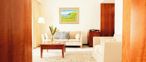 A modern living room with a beige sofa, a wooden coffee table, and a painting of a landscape on the wall.
