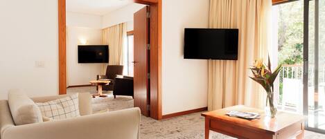 A hotel room with a sofa, a coffee table, a flat-screen TV, and a large window with curtains.