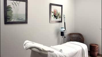 Relax in a serene spa room with a neatly made bed, wicker chair, and massage chair.