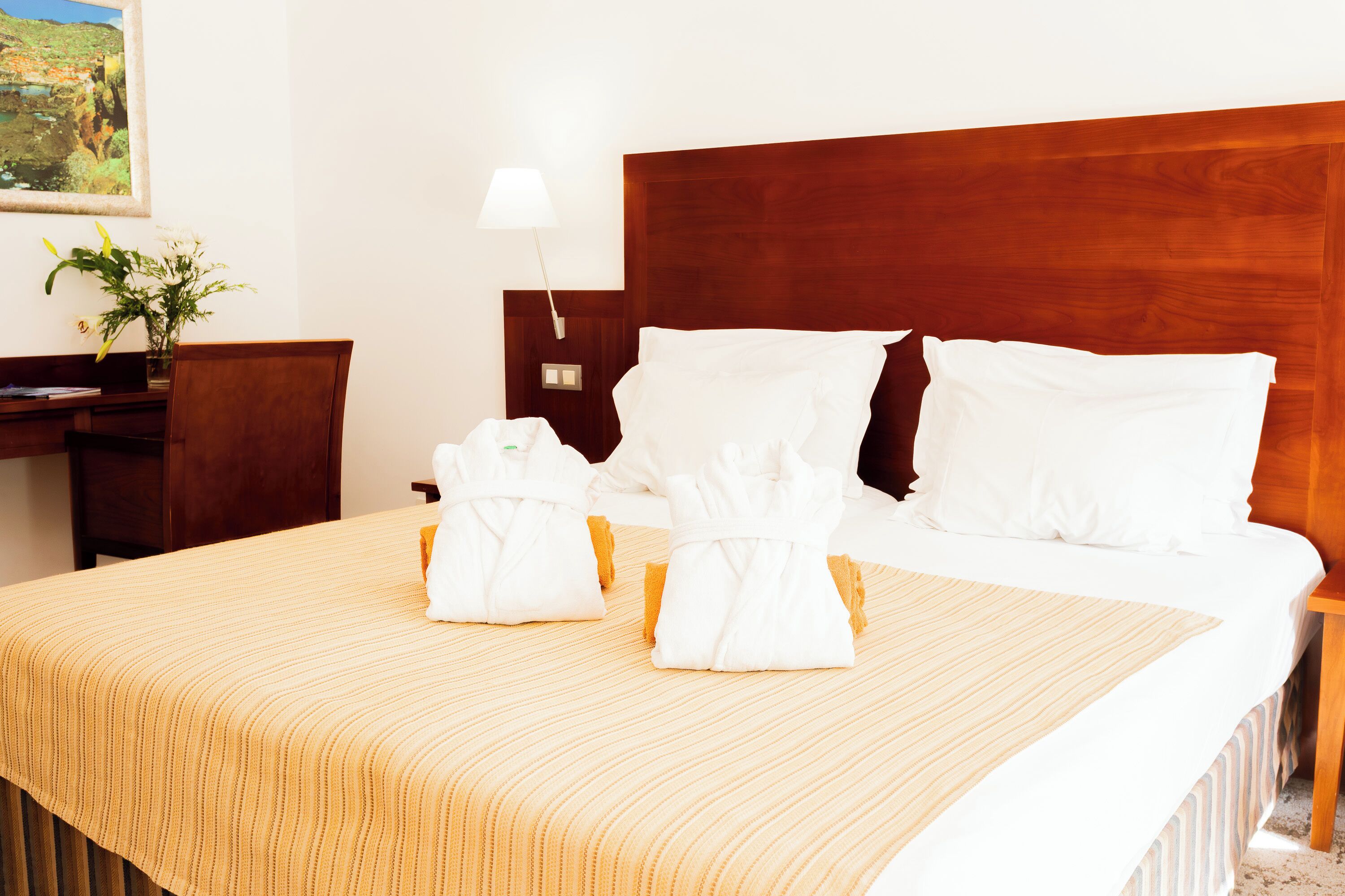 A neatly made bed with white linens and two towels folded at the foot.