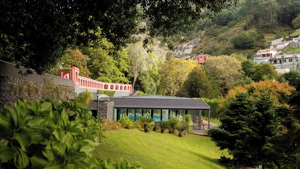 Ein modernes Gebäude mit Schwimmbad, umgeben von üppiger Vegetation und einer Steinmauer.