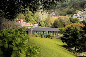 Ein modernes Gebäude mit Schwimmbad, umgeben von üppiger Vegetation und einer Steinmauer.
