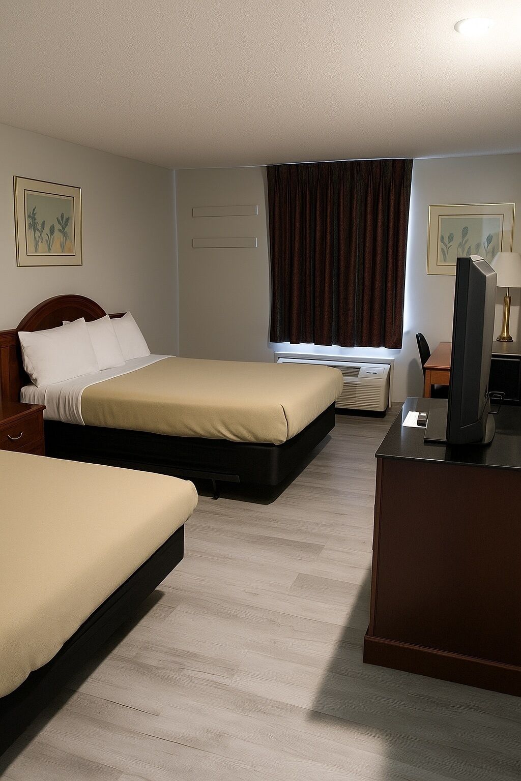 Ein Hotelzimmer mit zwei Betten, einem Schreibtisch mit Computer, einem Fernseher und einem Fenster mit Vorhängen.
