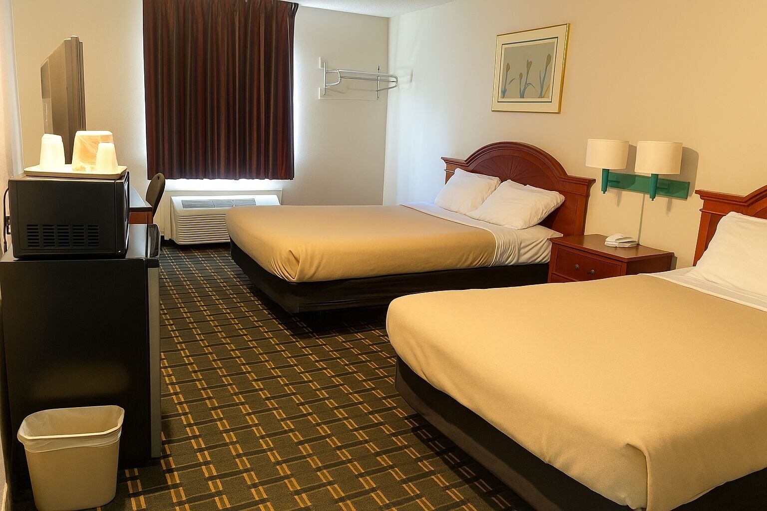 A hotel room with two beds, a desk with a computer, a trash bin, and a window with curtains.