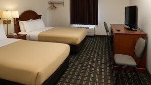 A hotel room with two beds, a desk with a television, a chair, a desk lamp, a bedside table with a phone, and a window with curtains.