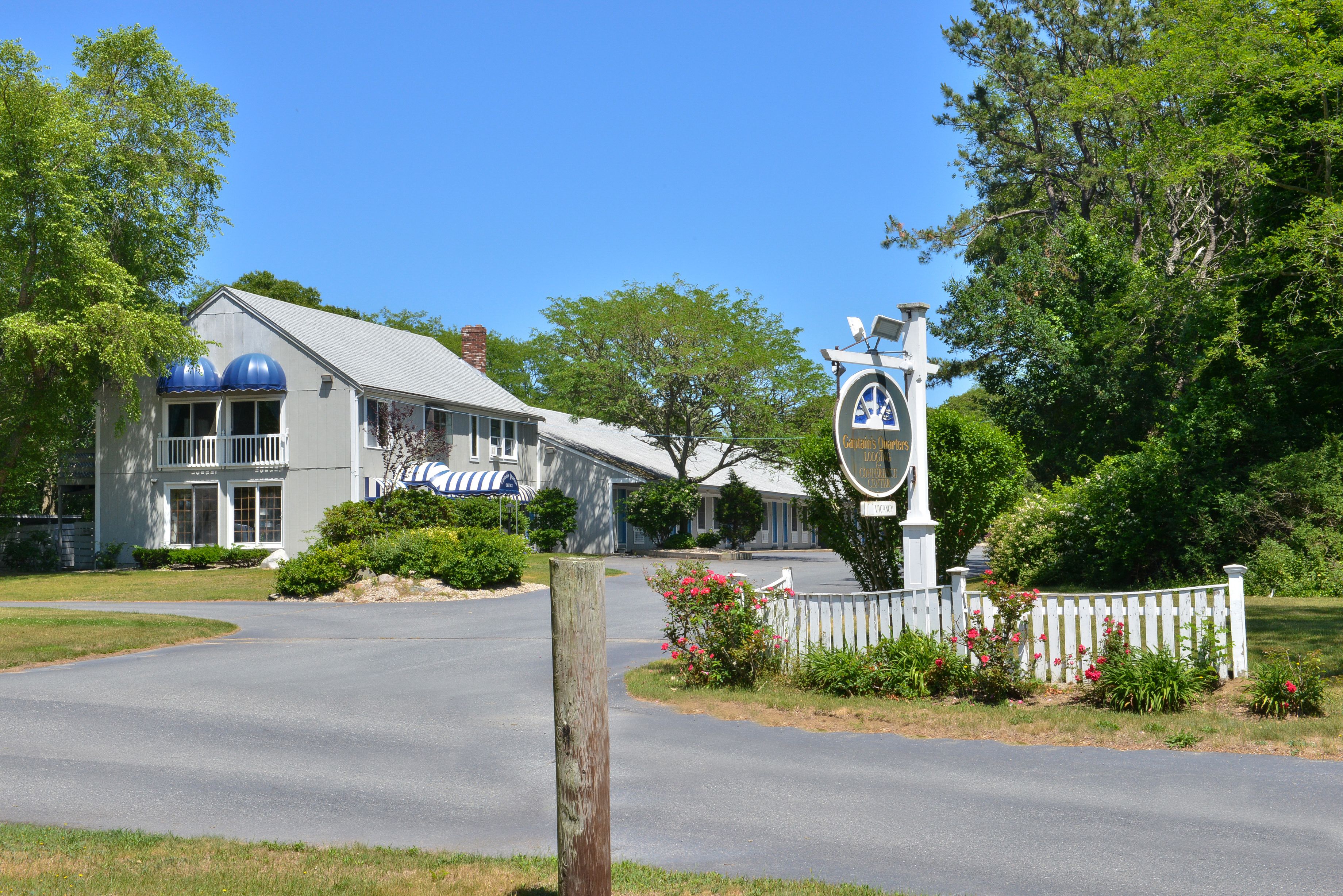 A two-story building with a white facade and blue accents, a covered porch, and a sign indicating it is a hotel.