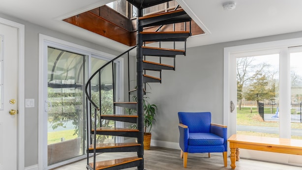 A modern interior with a spiral staircase, a blue chair, and a wooden bench. - Captains Quarters Motel & Conference Center (Eastham)