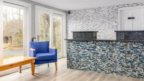 A modern kitchen with a mosaic backsplash, a blue chair, and a wooden table. - Captains Quarters Motel & Conference Center (Eastham)
