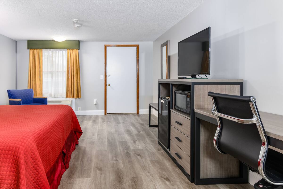 Hotellihuone, jossa on sänky, työpöytä tuolilla, televisio ja vaatekaappi.