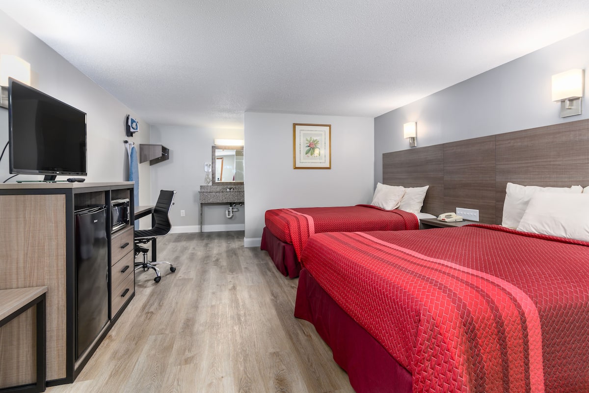 Hotellihuone, jossa on kaksi sänkyä, työpöytä, jossa on televisio, mikroaaltouuni ja pieni keittokomero.