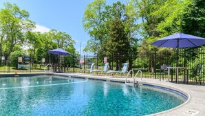 A swimming pool with lounge chairs and umbrellas, surrounded by a fence and trees. - Captains Quarters Motel & Conference Center (Eastham)