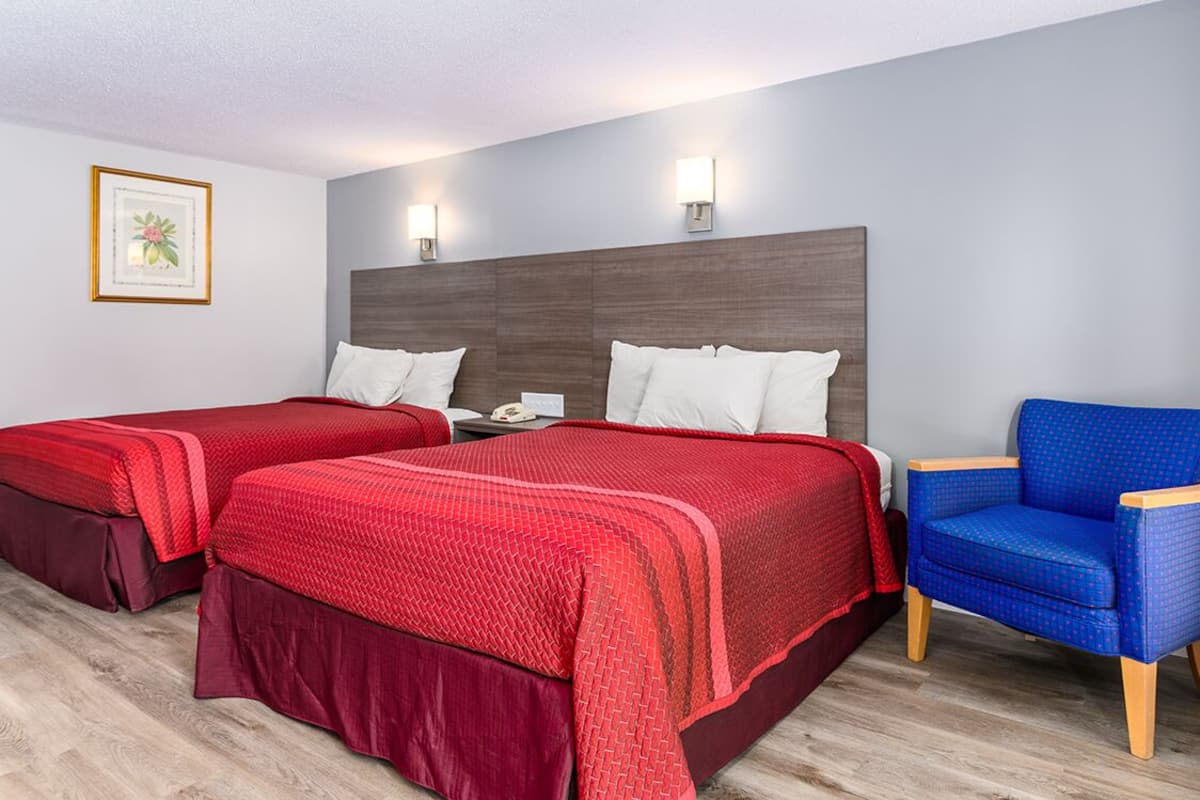 Hotellihuone, jossa on kaksi sänkyä, yöpöytä, tuoli ja seinällä oleva kehystetty kuva.
