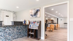 A modern reception area with a stone mosaic backsplash, a reception desk, and a dining area with wooden chairs and a table. - Captains Quarters Motel & Conference Center (Eastham)