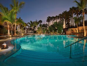 Uma grande piscina ao ar livre com design curvo, rodeada por palmeiras e espreguiçadeiras.