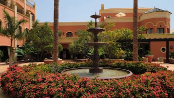 A courtyard with a central fountain surrounded by pink flowers and palm trees.