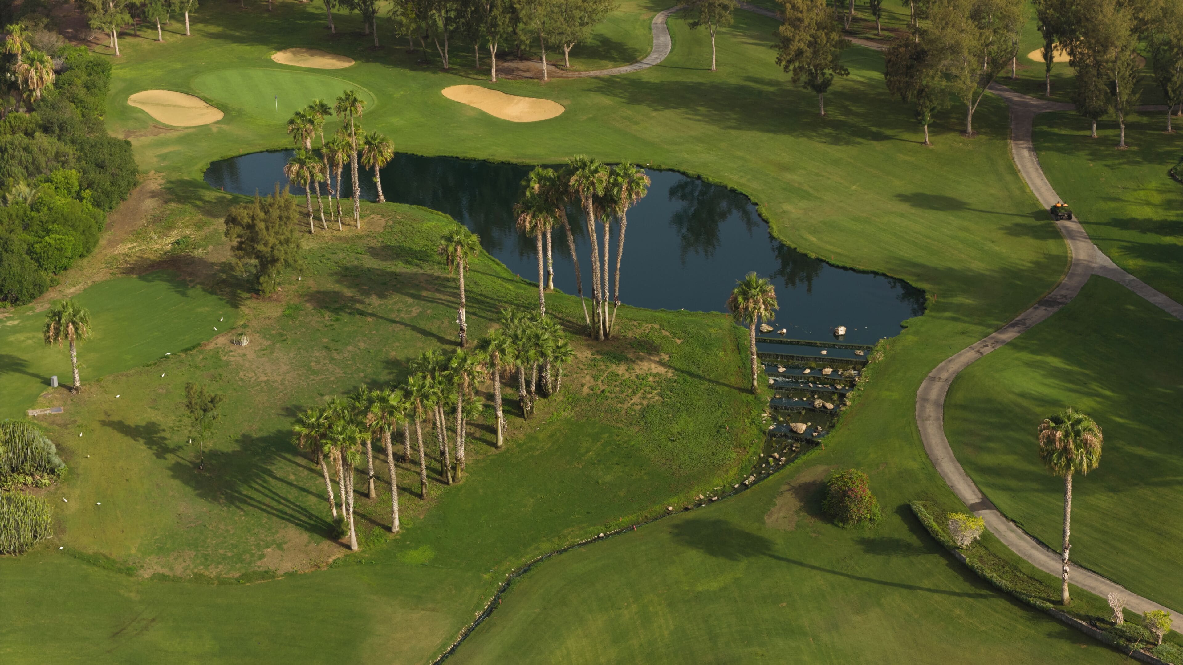 A golf course with a water hazard, sand bunkers, and a walking path.