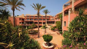 A hotel courtyard with palm trees, a central fountain, and a tiled floor.