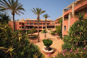 Un patio de hotel con palmeras, una fuente en el centro y suelo de baldosas.