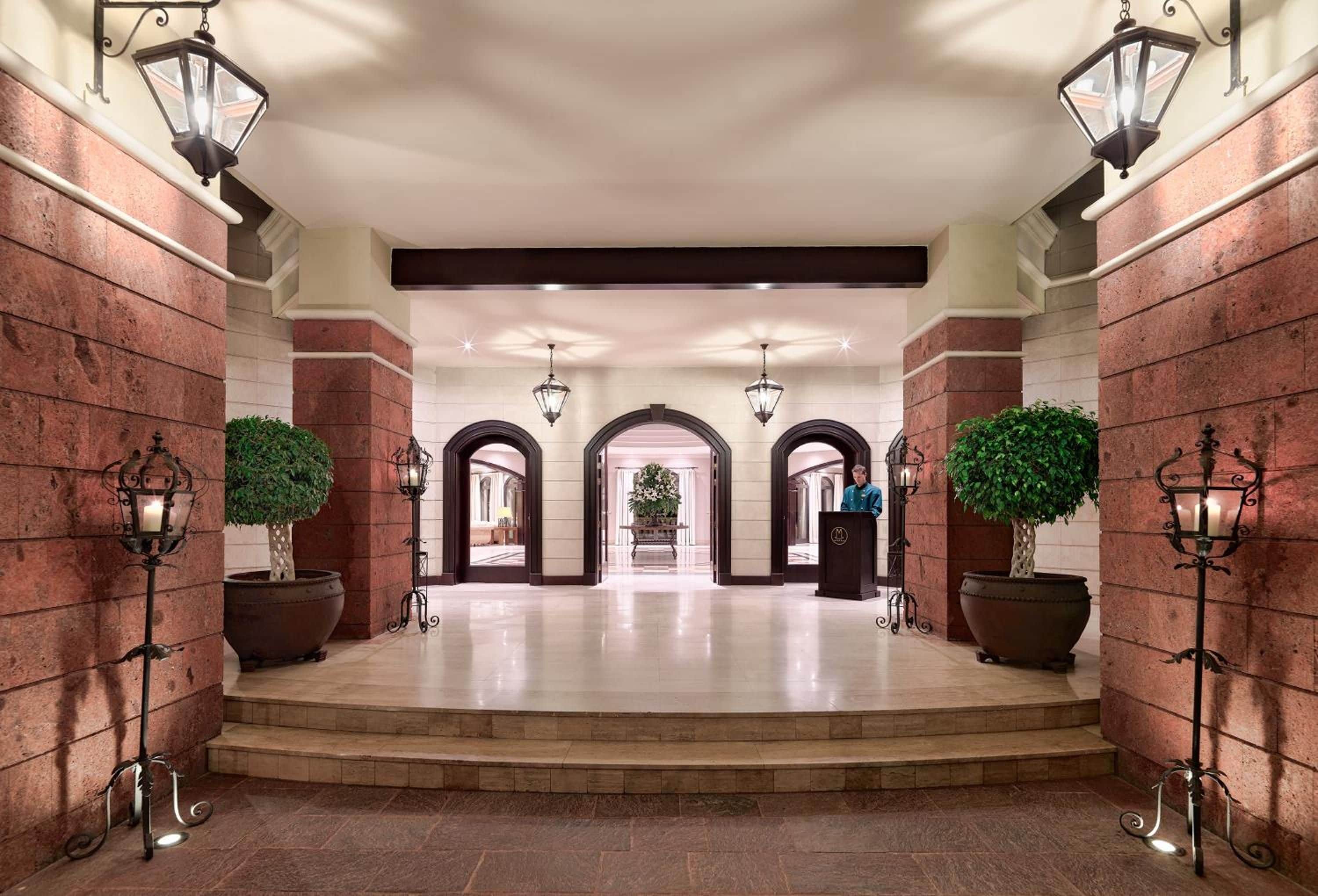 Un lobby de hotel imponente con piso de mármol, paredes de ladrillo rojo e iluminación decorativa.
