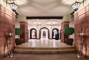 Un lobby de hotel imponente con piso de mármol, paredes de ladrillo rojo e iluminación decorativa.