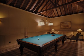 A pool table in a room with a high ceiling and wooden beams, a checkered floor, and two wall-mounted lamps.