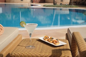 Een zwembadterras met een cocktailglas en een schaal amuse.'