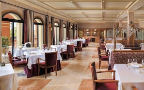 A spacious restaurant with multiple tables and chairs, large windows, and a classic interior design.