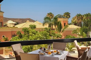 Een ontbijtruimte met een gedekte tafel, met uitzicht op een resort met palmbomen en een berg op de achtergrond.