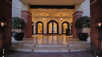 A hotel entrance with a grand archway, potted plants, and a reflective floor.