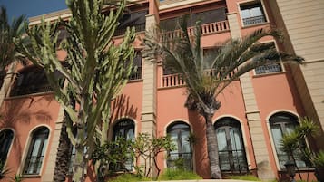 A multi-story building with balconies, windows with bars, and various plants including cacti and palm trees.