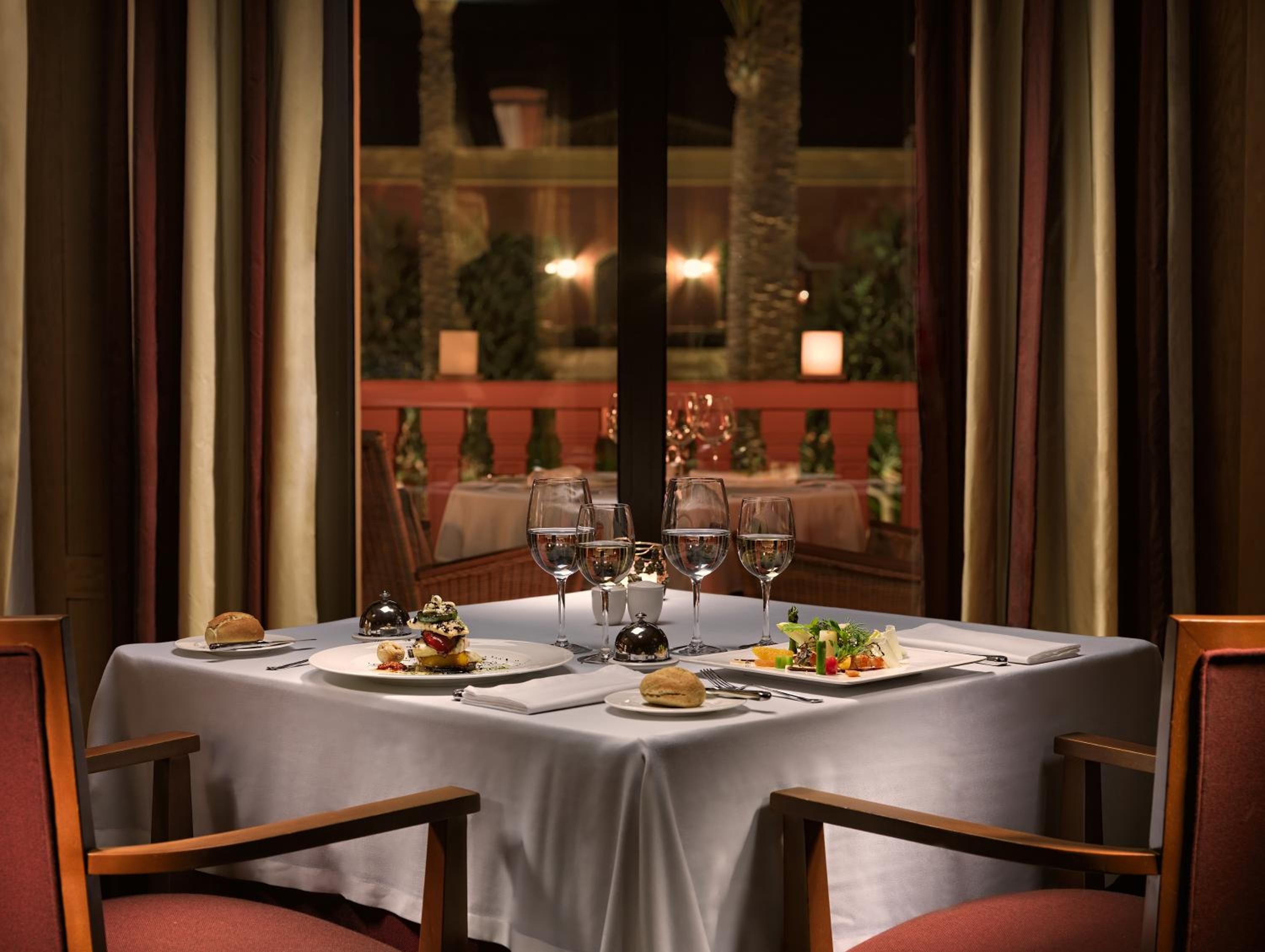 Mesa de comedor para cuatro personas, con platos de comida, vasos y cubiertos.