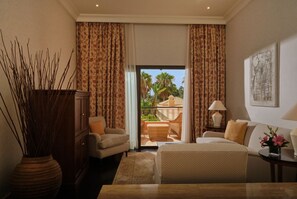Hotelkamer met een bed, een bank, een stoel, een tafel, een vaas met bloemen, een lamp, een schilderij aan de muur en uitzicht op het balkon.