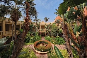 A courtyard with palm trees, a central fountain, and a building with a balcony.
