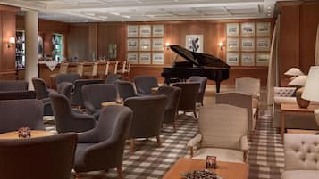 Un lobby de hotel con un piano de cola, varias zonas de estar, un bar y cuadros en las paredes.