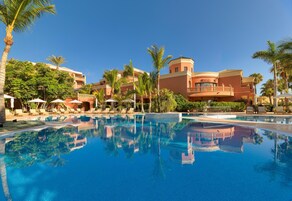 Un resort con una piscina grande, palmeras y un edificio con varios balcones.