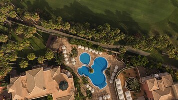 Vista aérea de un resort con piscina central, zonas de descanso y palmeras.