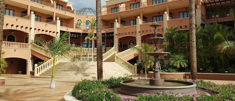 A multi-level hotel with a central fountain, palm trees, and a staircase.
