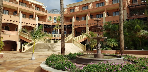 A multi-level hotel with a central fountain, palm trees, and a staircase.
