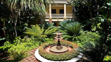 Un patio con una fuente central, rodeado de abundante vegetación y un edificio con balcón.