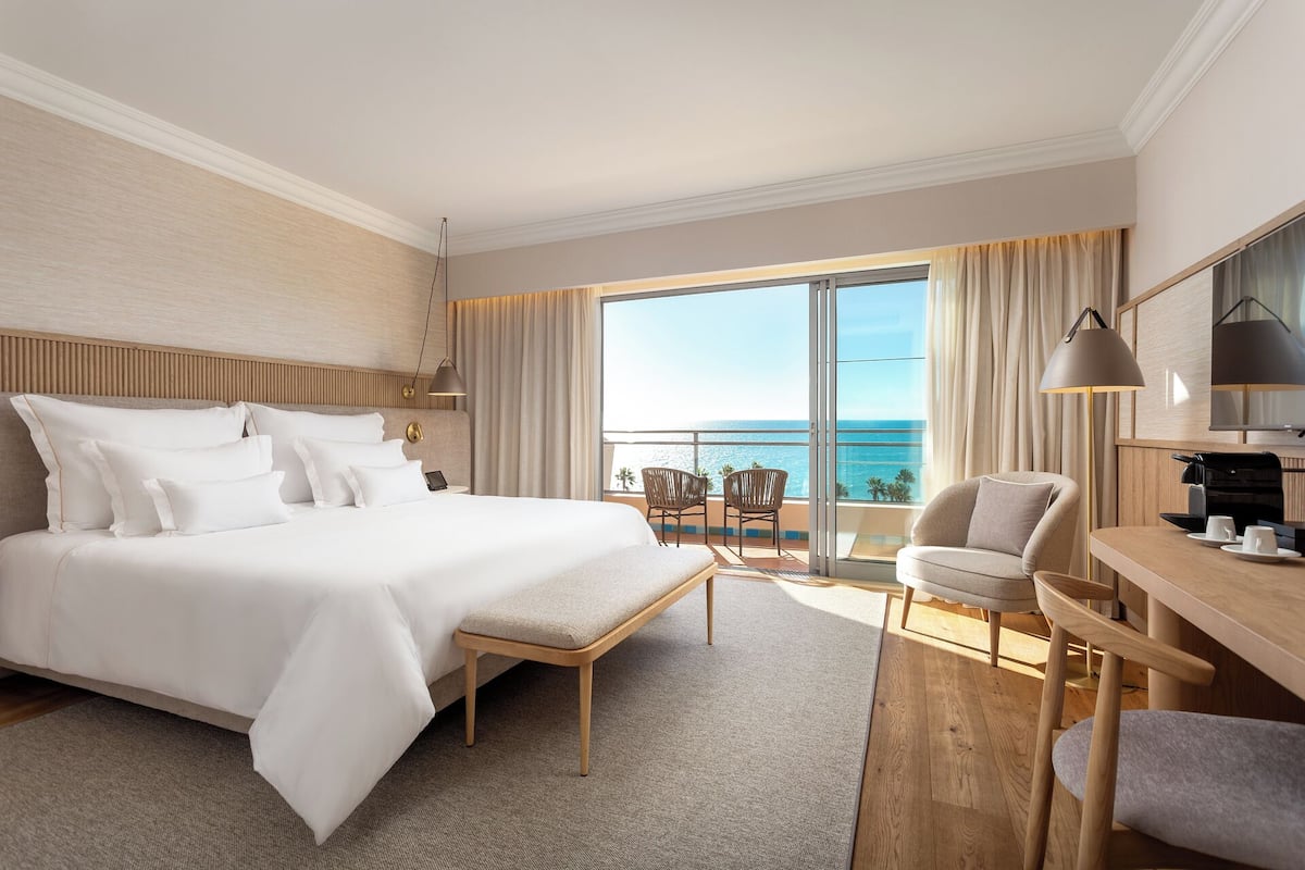 A hotel room with a large bed, a desk, a chair, and a view of the ocean.