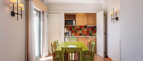 A dining area with a green table and chairs, a kitchen with colorful tiles, and a microwave.