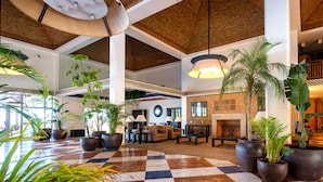 A spacious lobby with a checkered floor, large potted plants, comfortable seating, and a fireplace.
