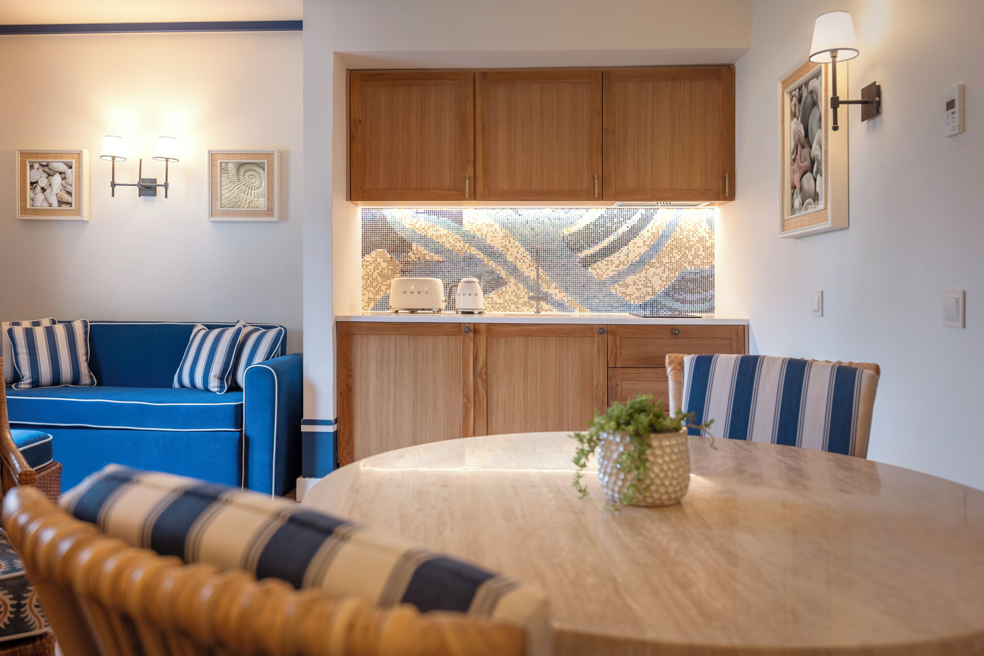 Une cuisine moderne avec des meubles en bois, un canapé bleu, une table à manger avec des chaises à rayures et des luminaires fixés au mur.