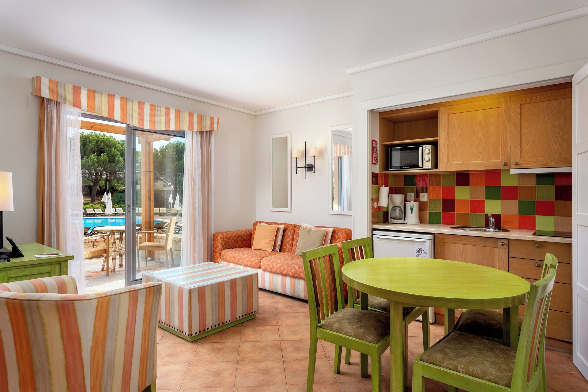 Una sala acogedora con sofá, sillas, una mesa de comedor y una cocina con baldosas de colores.