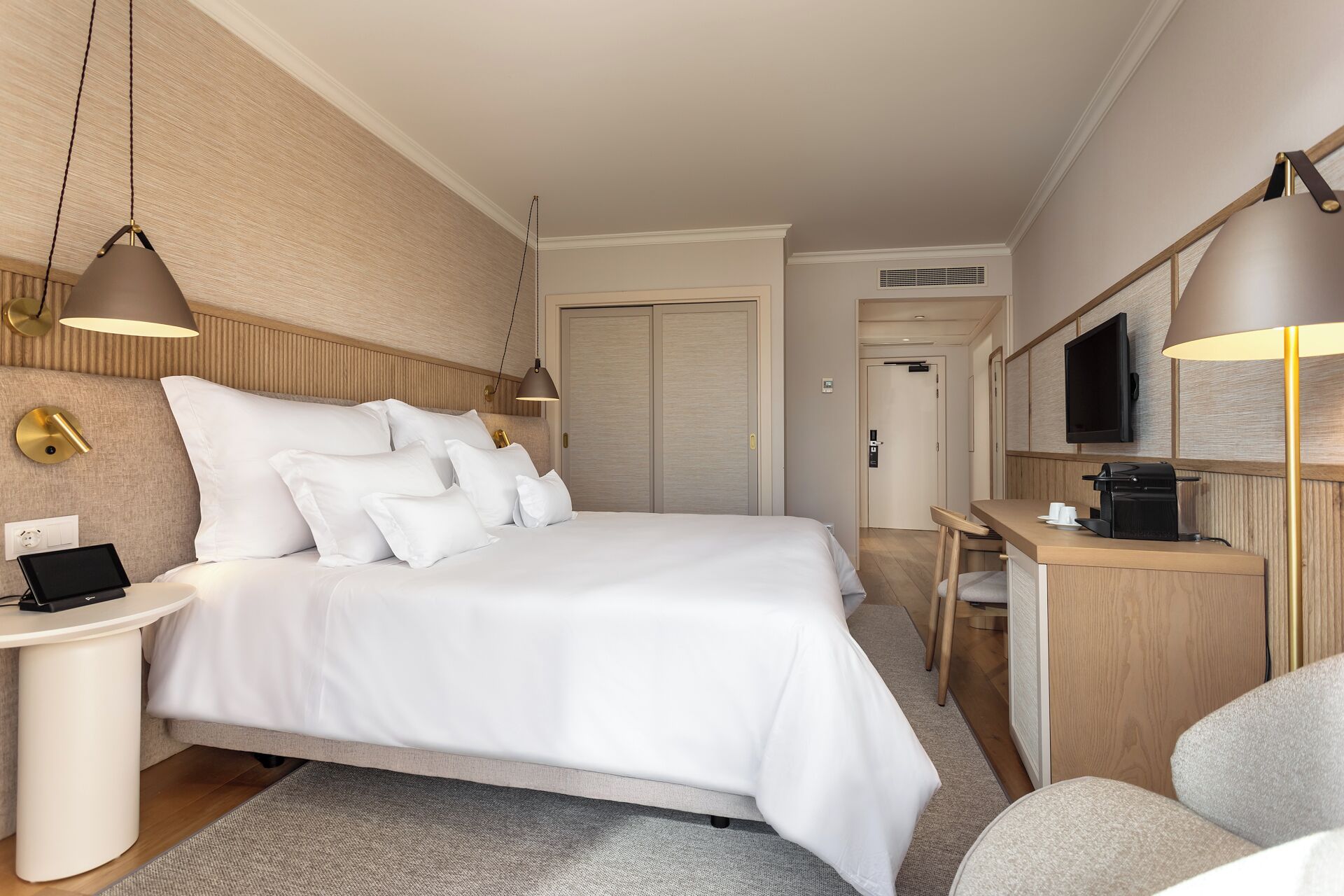 A hotel room with a large bed, bedside tables, a desk, a chair, a TV, and a wardrobe.