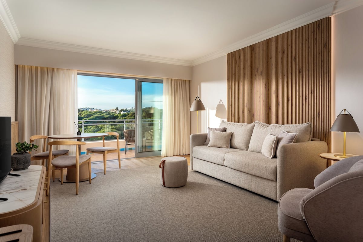 A modern living room with a sofa, armchairs, a TV, and a balcony with a view.