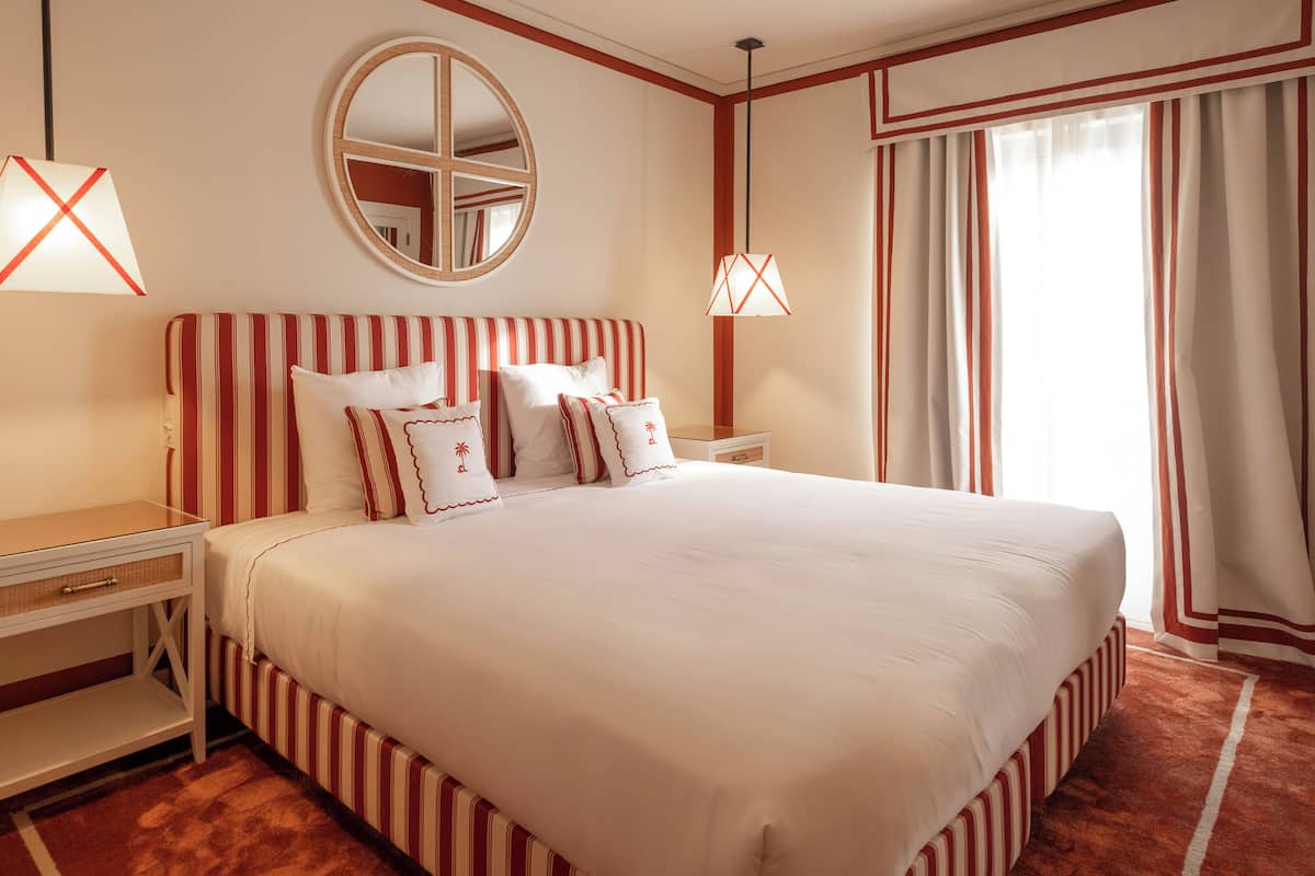 A neatly arranged hotel room with a large bed, a bedside table, a mirror, and a window with curtains.