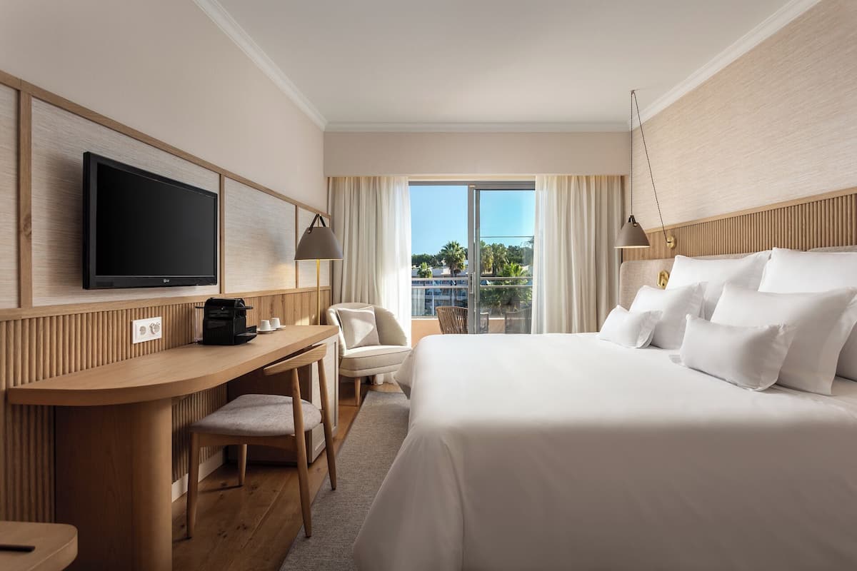 A hotel room with a bed, a desk with a TV, a chair, and a view of the outdoors.