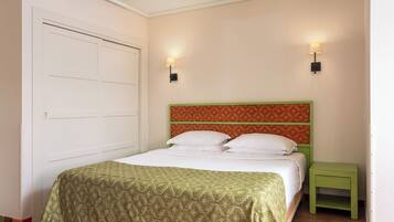 A bedroom with a bed, a green nightstand, two wall-mounted lights, and a white door.