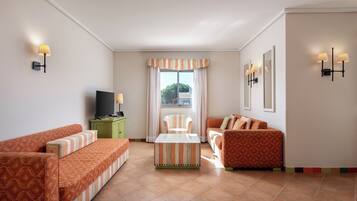 A hotel room with striped sofas, a small green cabinet, a TV, and a window with curtains.